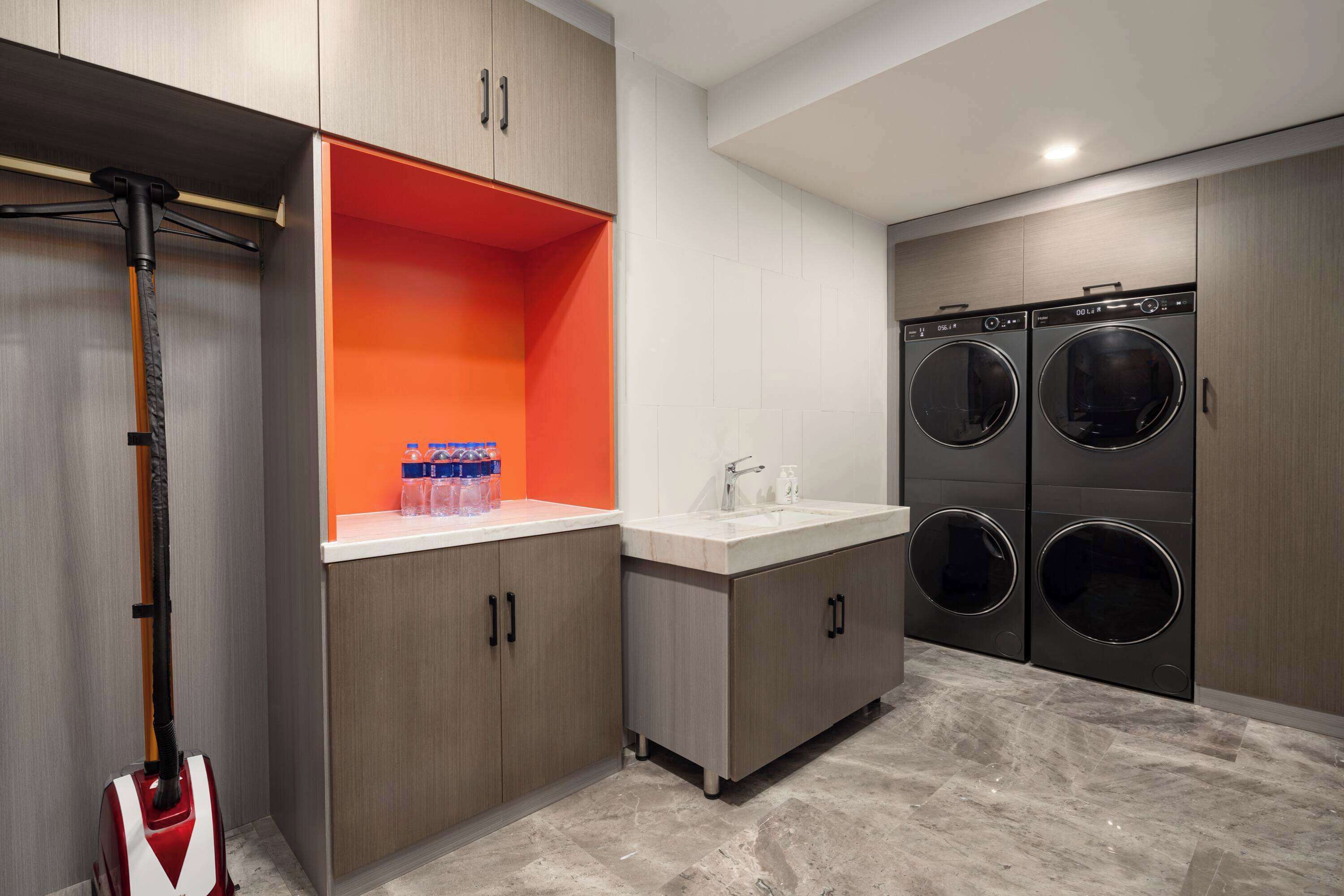 A modern laundry room with two wall-mounted washing machines, a sink, and a vacuum cleaner.