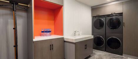 A modern laundry room with two wall-mounted washing machines, a sink, and a vacuum cleaner.