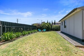Relax in the serene backyard with a beautifully maintained lawn and garden, perfect for outdoor dining or unwinding in the two comfortable chairs.