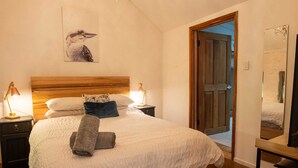 A bedroom with a wooden headboard, a bed with white bedding, two bedside lamps, a wall-mounted picture, a door leading to another room, and a mirror on the wall.