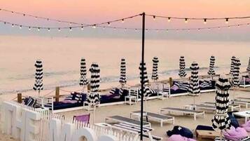 A beachside setting with striped umbrellas and lounge chairs, a white fence with the word "MOSFLEV" on it, and a string of lights in the background.