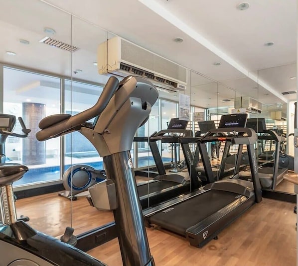 Une salle de sport équipée de tapis de course, de vélos d’appartement et d’un appareil d’aviron.