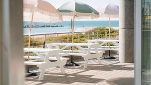 Une terrasse avec des tables et des chaises blanches, et trois parasols pour faire de l’ombre.