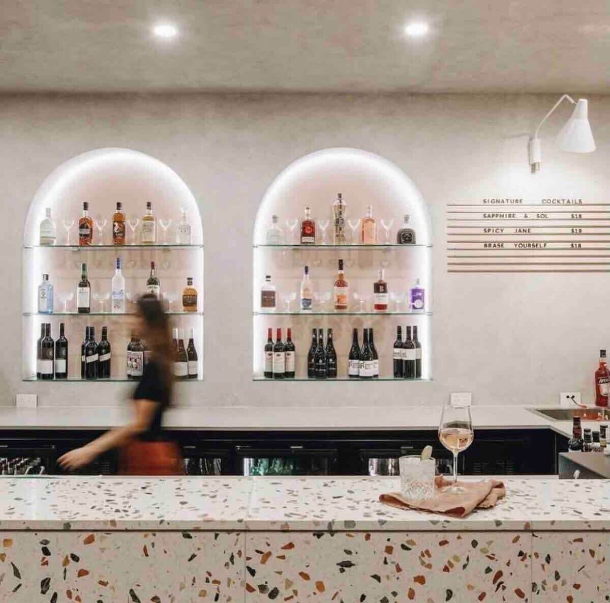 A bar area with shelves of liquor bottles, a menu board, and a bar counter.