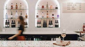 Un espace bar avec des étagères remplies de bouteilles d’alcool, un tableau affichant le menu et un comptoir.