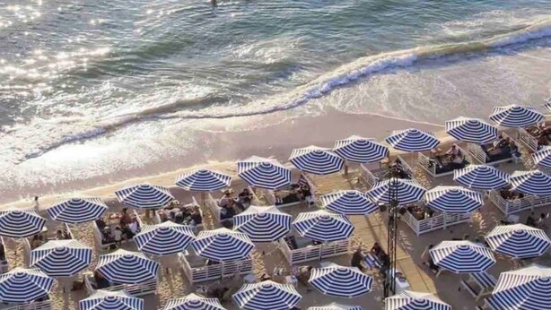 Une plage bordée de rangées de parasols rayés et de chaises longues, ce qui indique qu’il s’agit d’un complexe hôtelier en bord de mer.