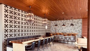 Eine moderne Bar mit Holzbalkendecke, Wand mit Muster und einer langen Theke mit Barhocker.