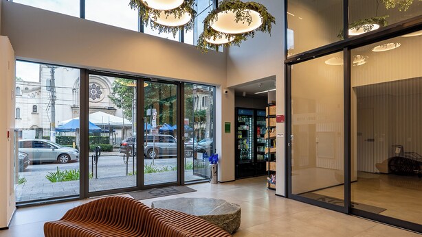 A modern lobby with a large glass door, a seating area with a unique wavy-patterned sofa, and a view of the street outside. - Alameda Lorena, 718- Jardim Paulista (São Paulo)