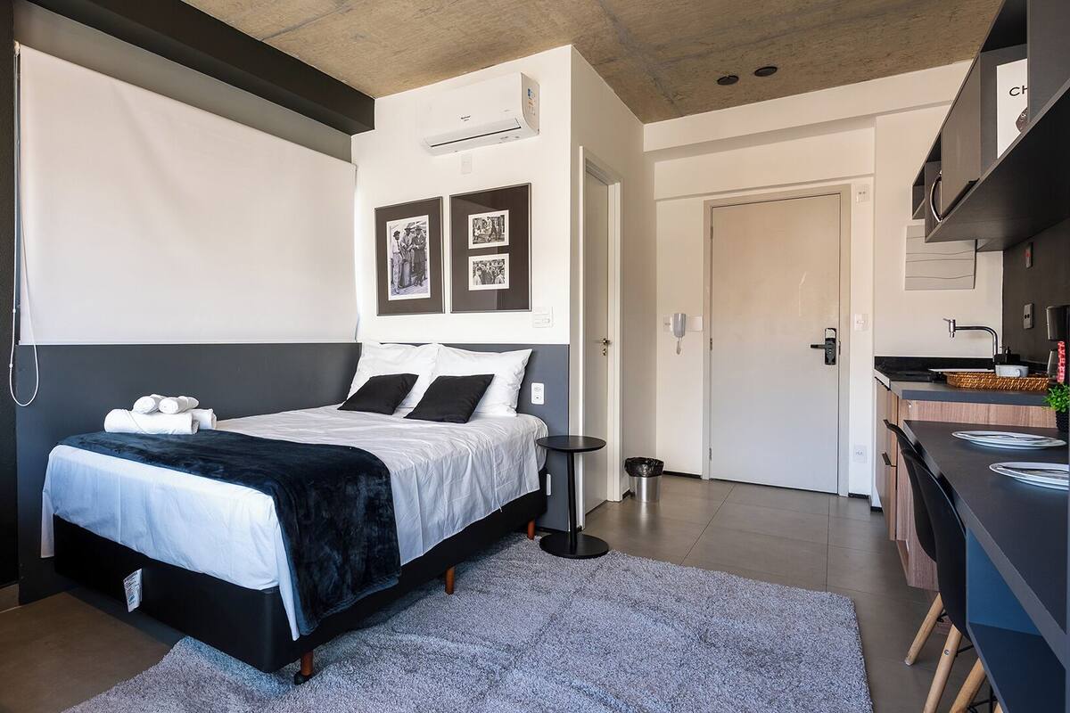 Ein modernes Schlafzimmer mit Bett, Nachttischen, einem kleinen runden Tisch und einer Küchenzeile mit Spüle und Herd.
