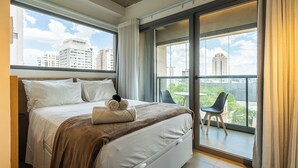 A hotel room with a large bed, a view of the city through floor-to-ceiling windows, and a balcony with a chair. - Alameda Lorena, 718- Jardim Paulista (São Paulo)