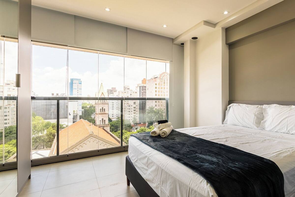 Ein modernes Schlafzimmer mit großem Fenster, einem Bett mit weißen Bettwäsche und Blick auf die Stadt.