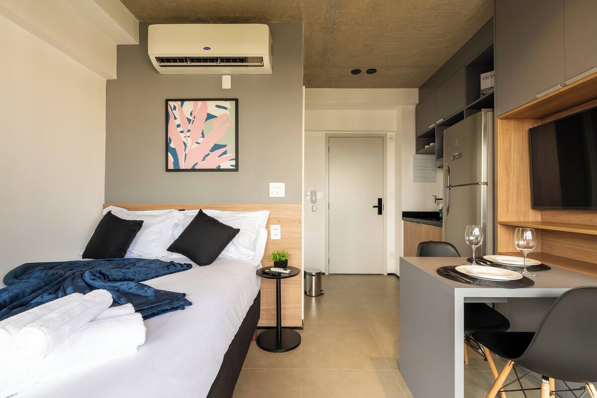 Ein modernes Hotelzimmer mit Bett, Nachttisch und einer kleinen Küchenzeile.
