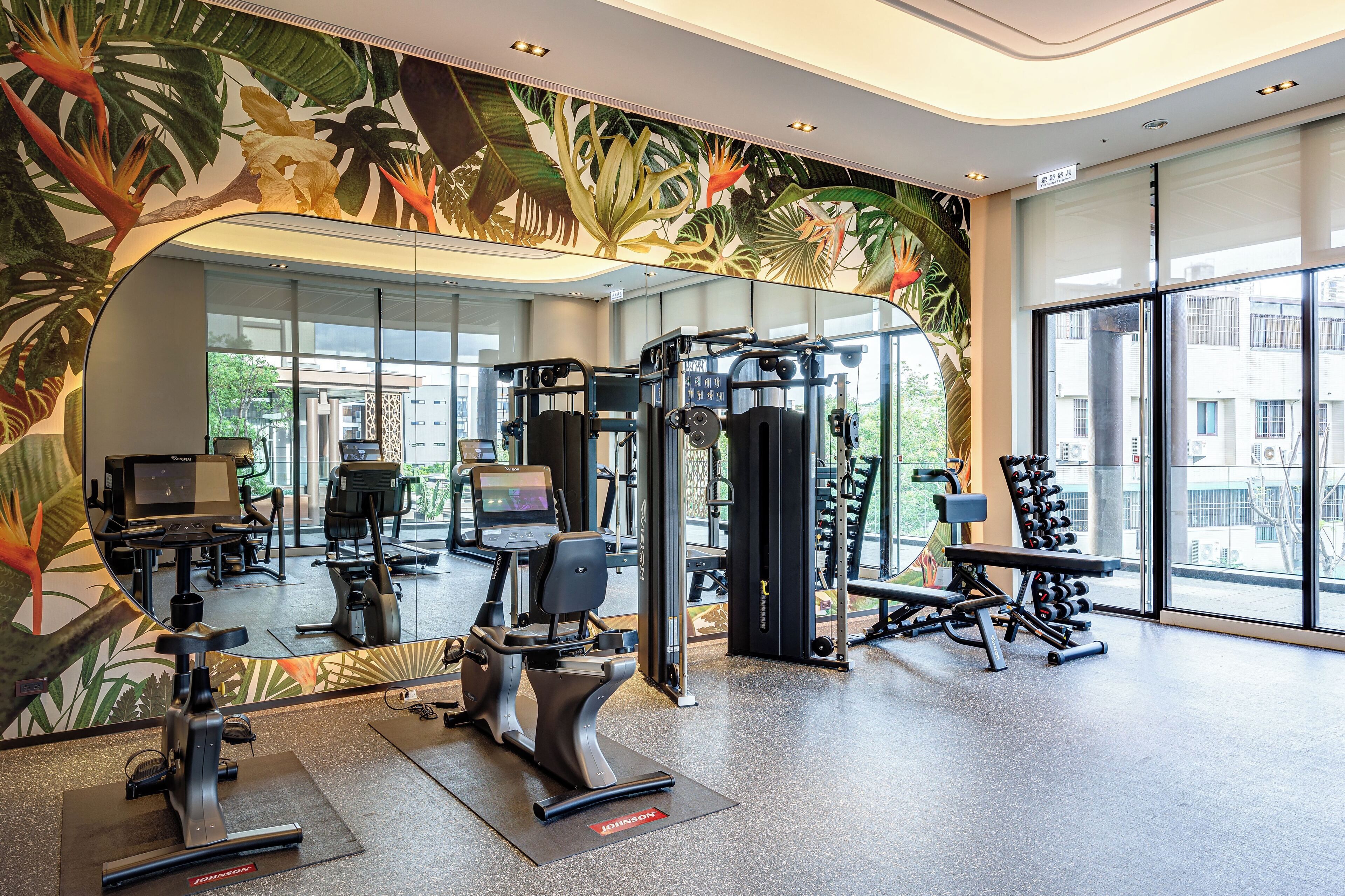 A gym with exercise equipment, a large mirror, and a tropical mural.