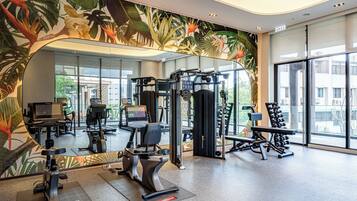 A gym with exercise equipment, a large mirror, and a tropical mural.