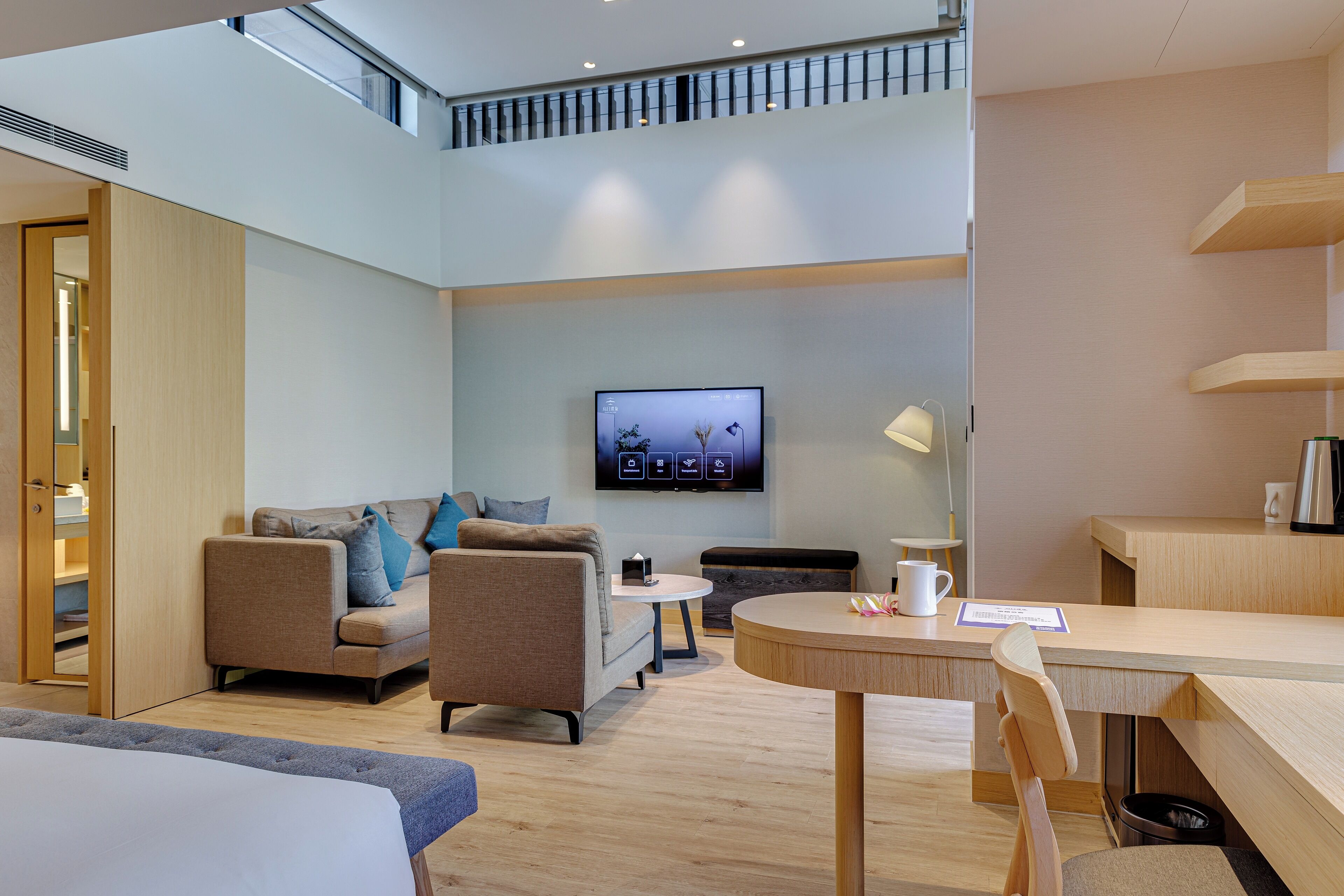 A modern hotel room with a sofa, a round table, a TV mounted on the wall, and a balcony.