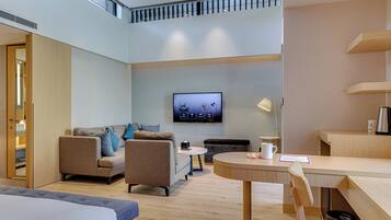 A modern hotel room with a sofa, a round table, a TV mounted on the wall, and a balcony.