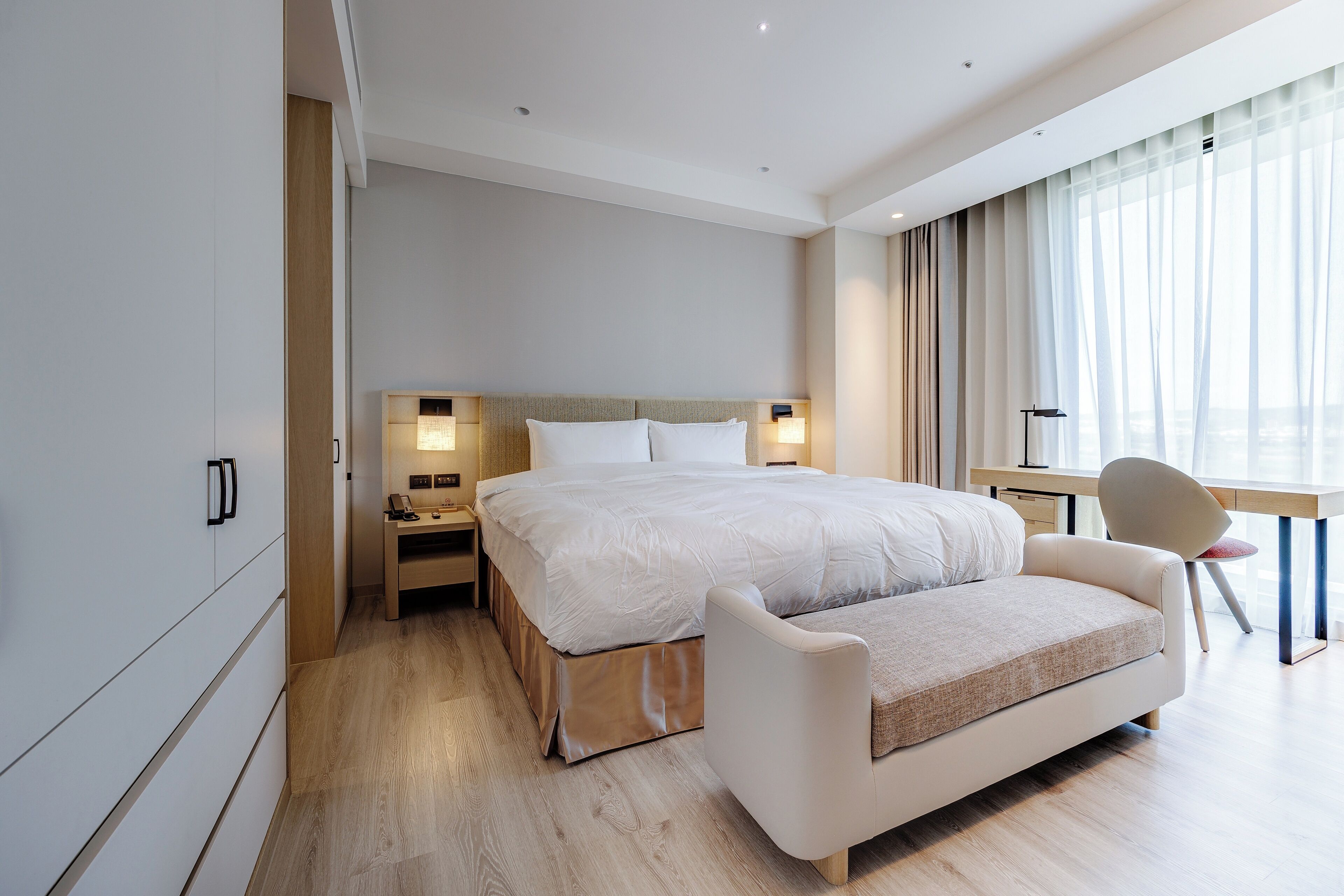 A modern hotel room with a large bed, bedside tables, a desk, and a chair.