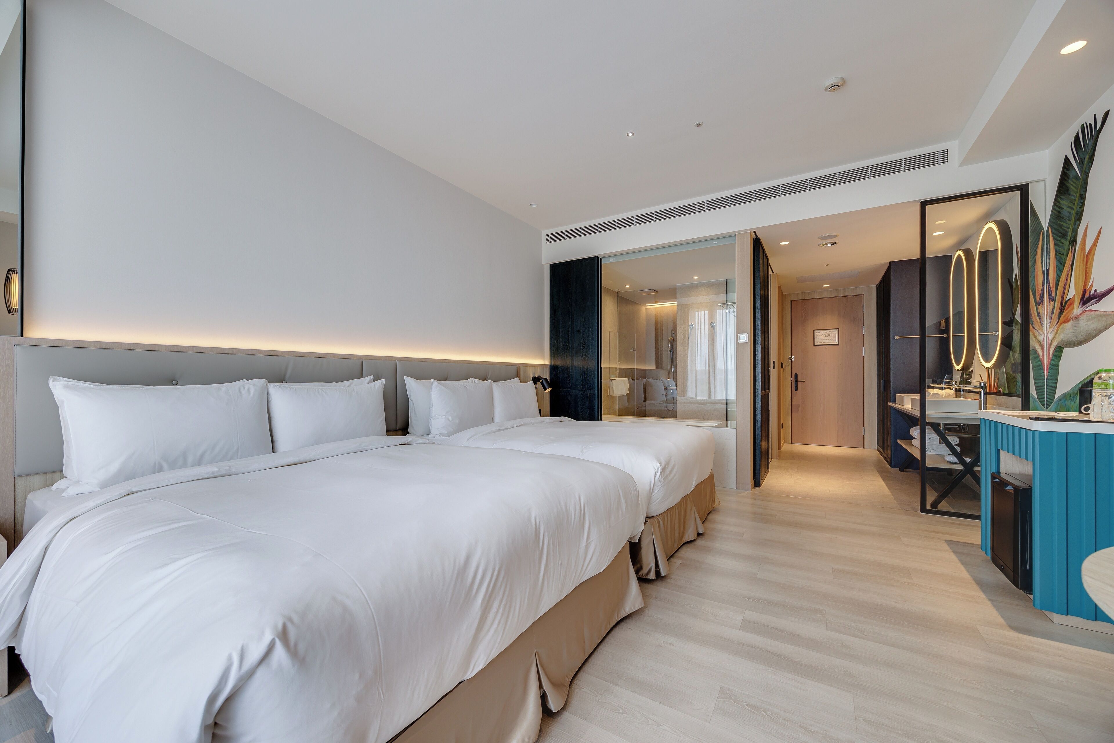 A modern hotel room with a large bed, a desk with a chair, and a glass partition.