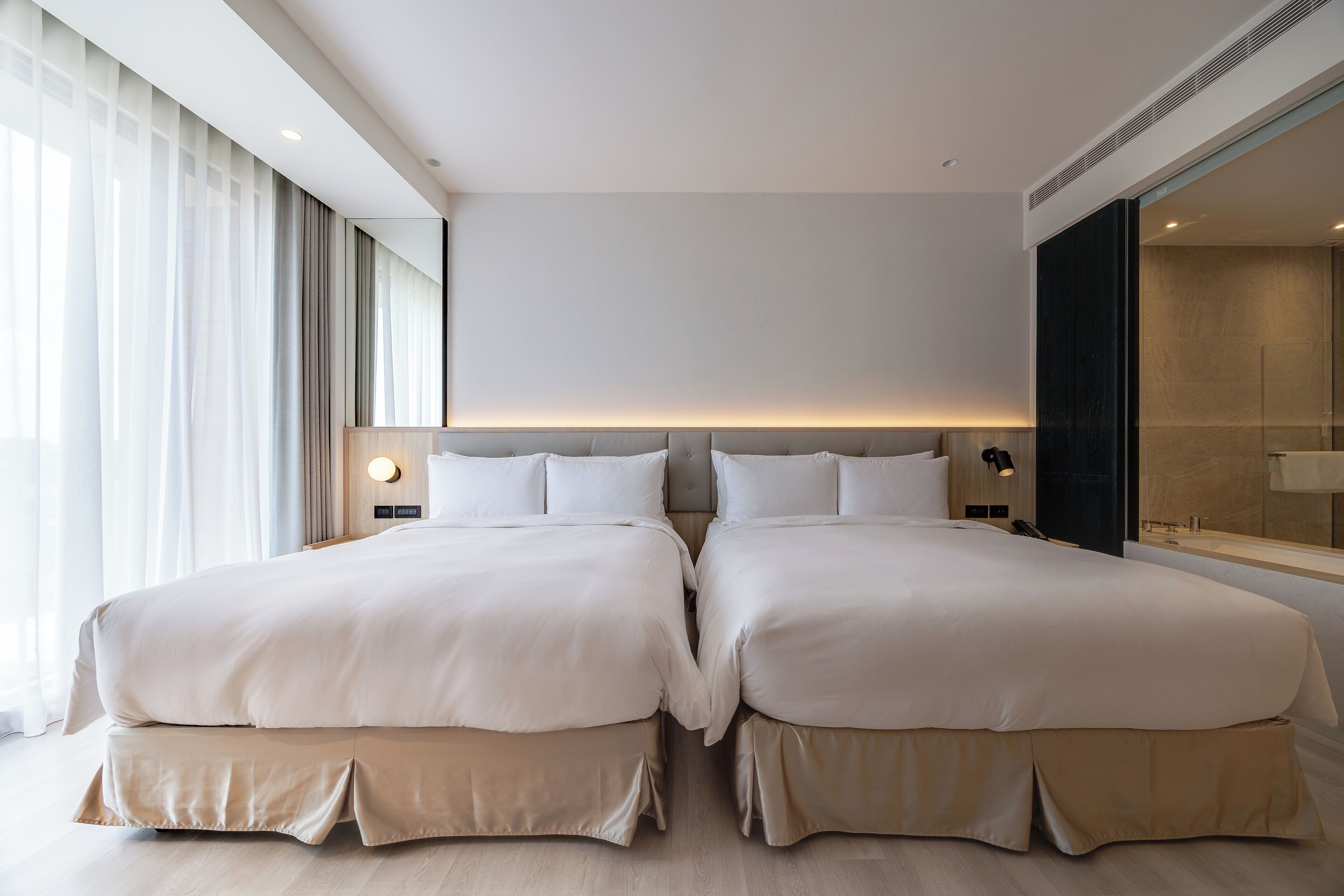 Moderni hotellihuone, jossa on kaksi suurta sänkyä, suuri peili ja näkymä kaupunkiin.