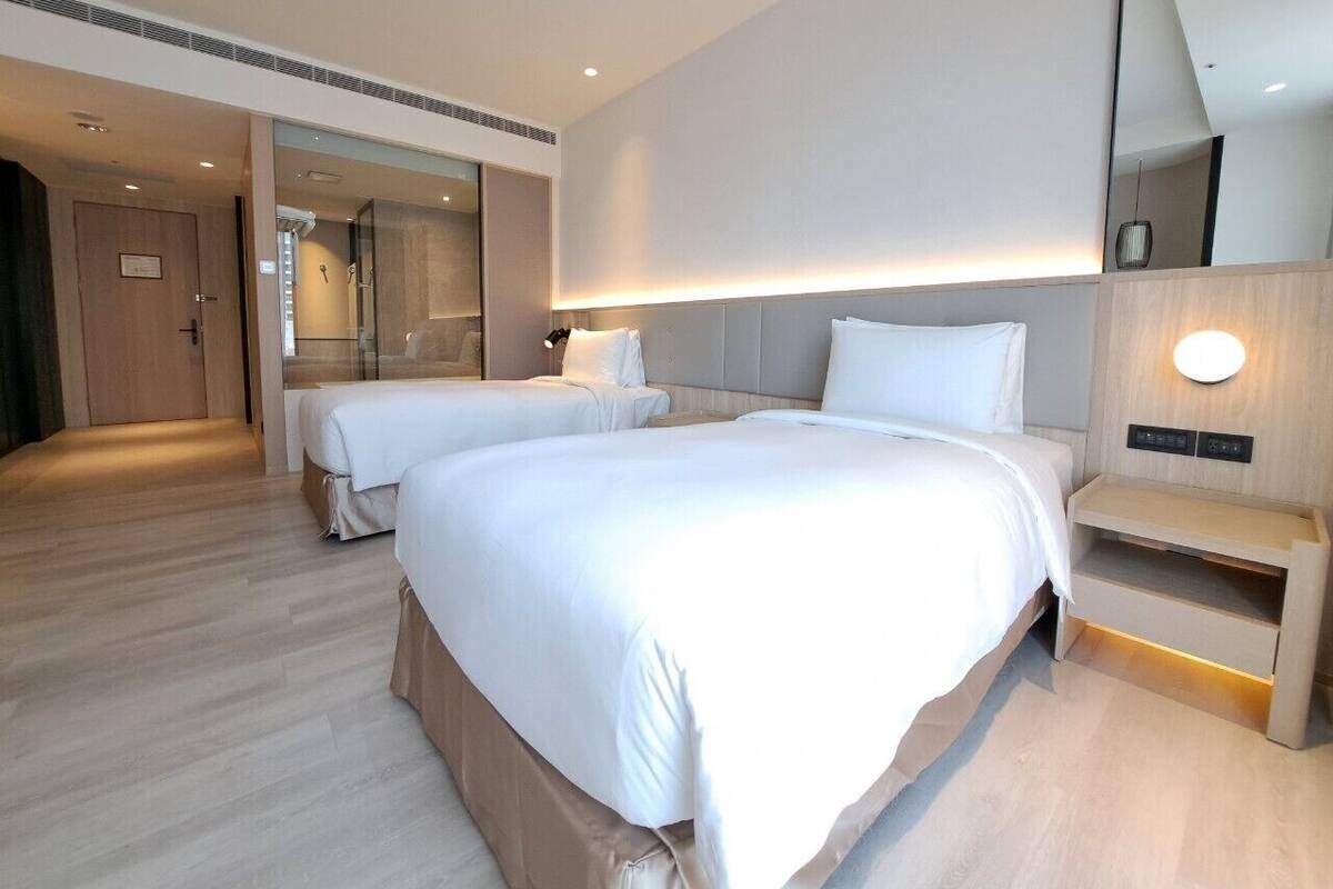 Une chambre d’hôtel moderne avec deux lits, un grand miroir et une table de chevet avec une lampe.