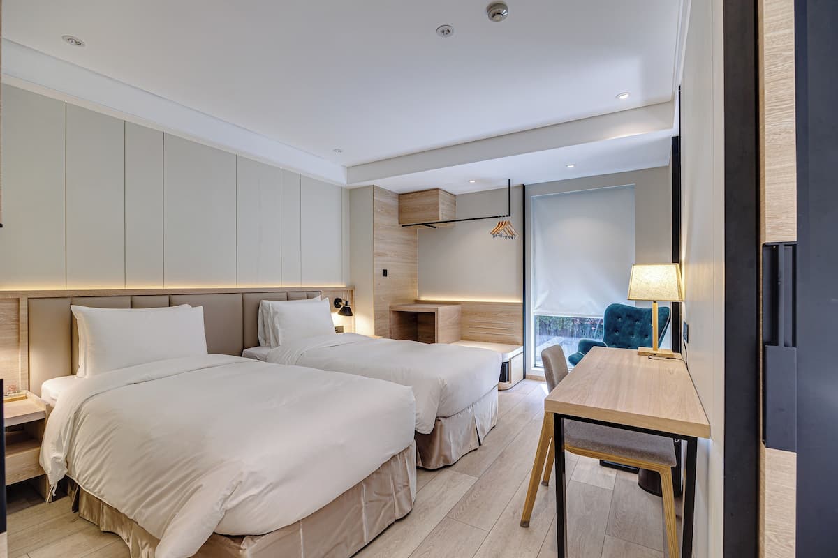 Une chambre d’hôtel moderne avec deux lits, une table en bois et une grande fenêtre donnant sur un paysage agréable.