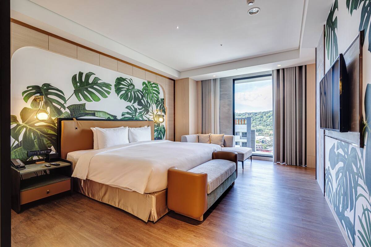Une chambre d’hôtel moderne avec un grand lit, un canapé, un bureau avec une lampe et une télévision.