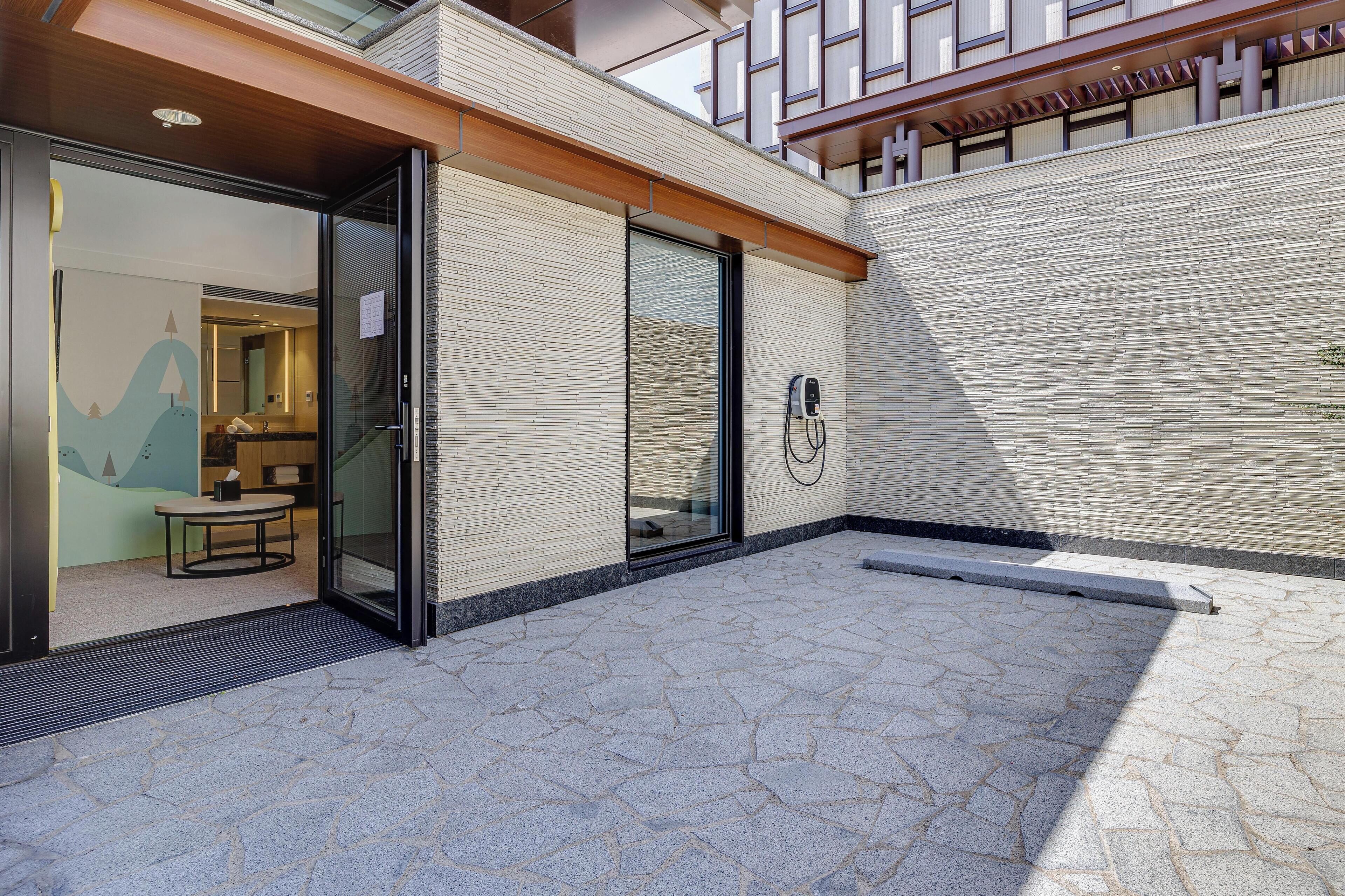 A modern building with a glass entrance, a small outdoor seating area, and a visible electrical outlet.