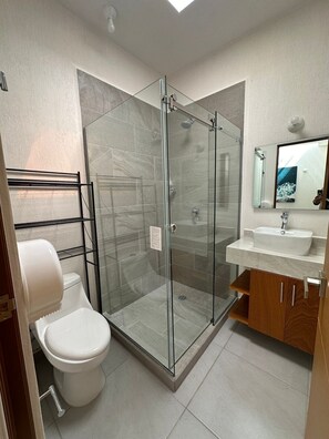 A modern bathroom with a glass-enclosed shower, a toilet, a sink, and a mirror. - Puerto Vallarta Altavela Egina 57 (Valle de Banderas)
