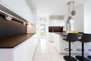 Een moderne keuken met witte kasten, een zwart aanrecht en een bar voorzien van twee zwarte barkrukken.