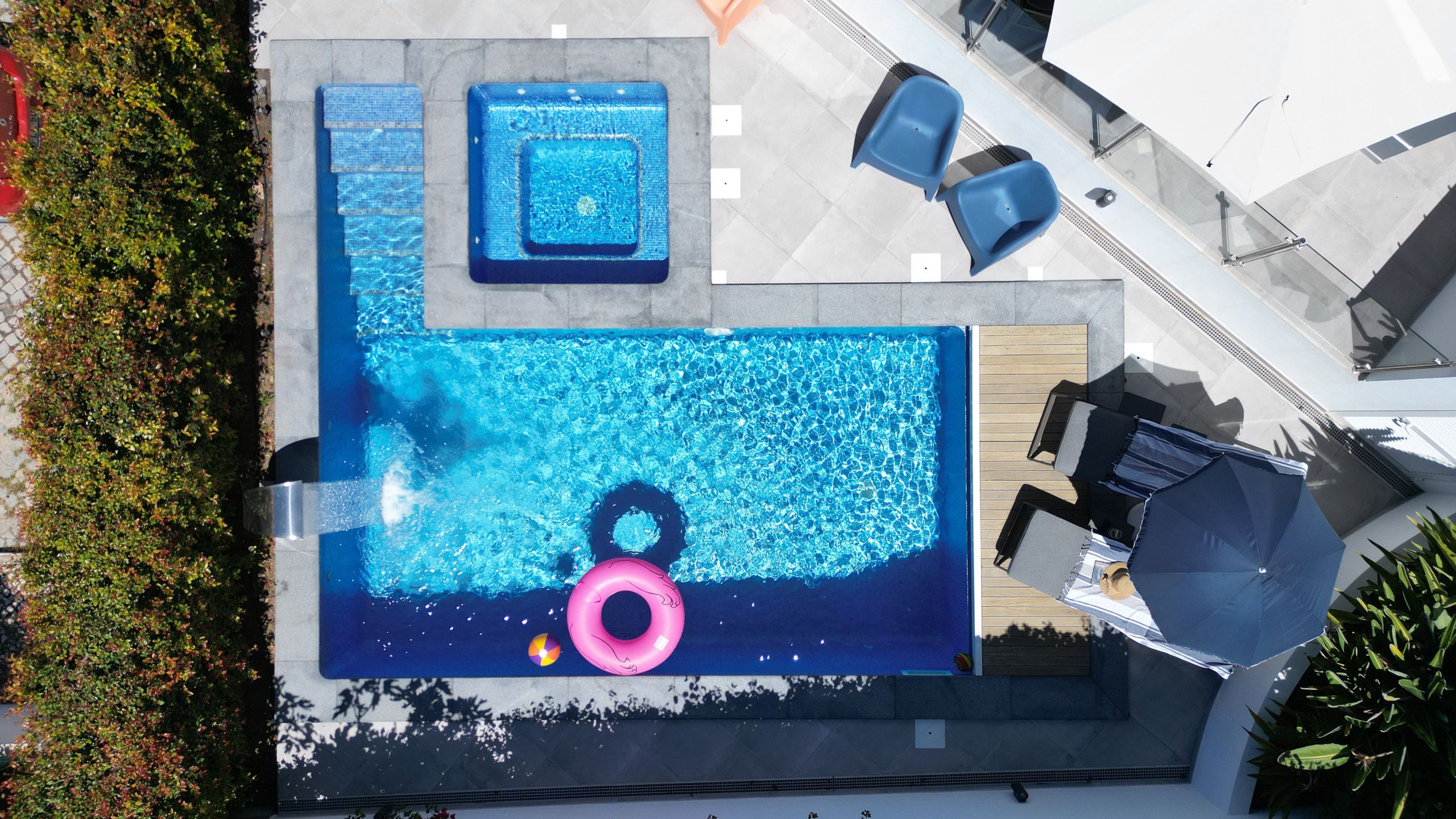 An aerial view of a swimming pool with a hot tub, lounge chairs, and a deck area.