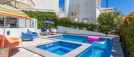 A swimming pool with two separate sections, surrounded by a patio area with lounge chairs and umbrellas.