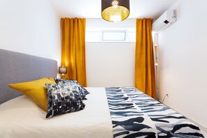 Een hotelkamer met een bed, een nachtkastje, een lamp, een raam met gordijnen en een airconditioning.
