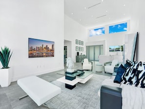A modern living room with a cityscape painting, a glass coffee table, white sofas, and a staircase leading to an upper level.