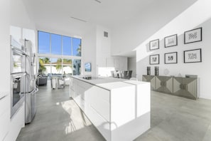 A modern kitchen with a large island, stainless steel appliances, and a view of palm trees.