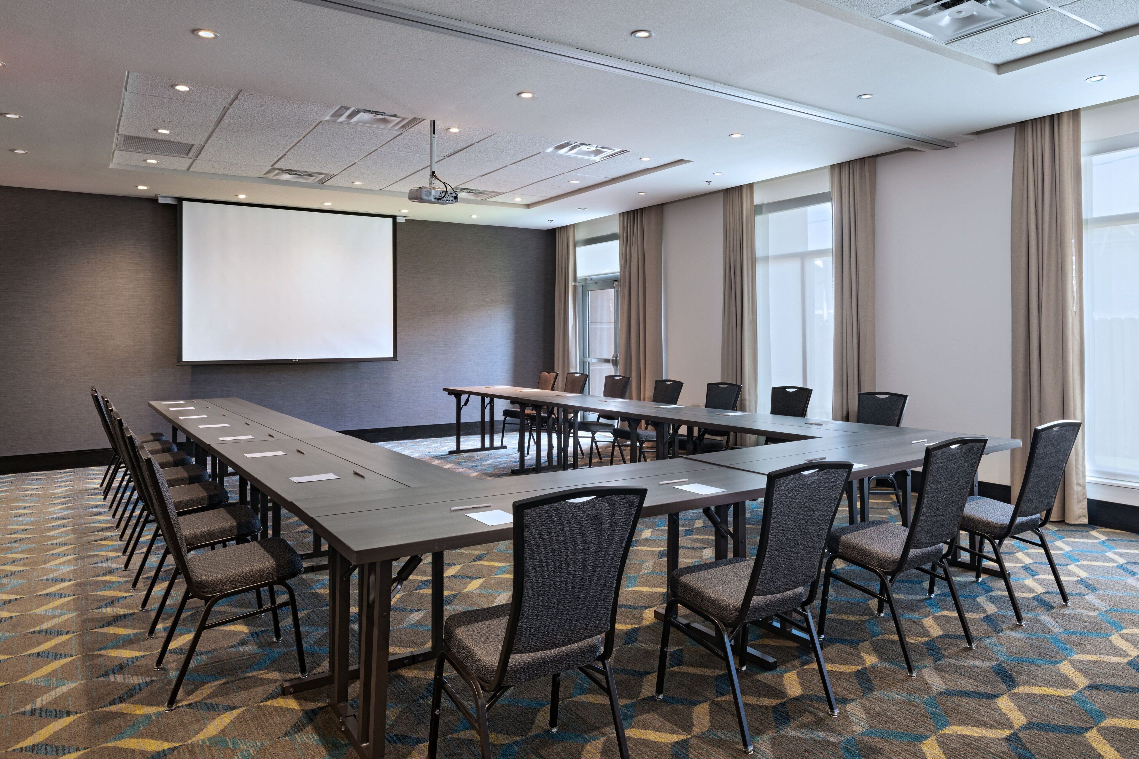 Une salle de conférence avec une longue table, des chaises, un écran de projection et un sol recouvert de moquette.