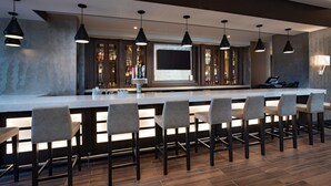 Un espace bar moderne doté d’un long comptoir, de nombreux tabourets, d’un éclairage suspendu et d’un grand écran.