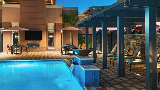 Une piscine avec des chaises longues et des parasols, un foyer extérieur et un mur en pierre.