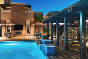 A swimming pool with lounge chairs and umbrellas, a fire pit, and a stone wall. - Residence Inn Corpus Christi South (Corpus Christi)