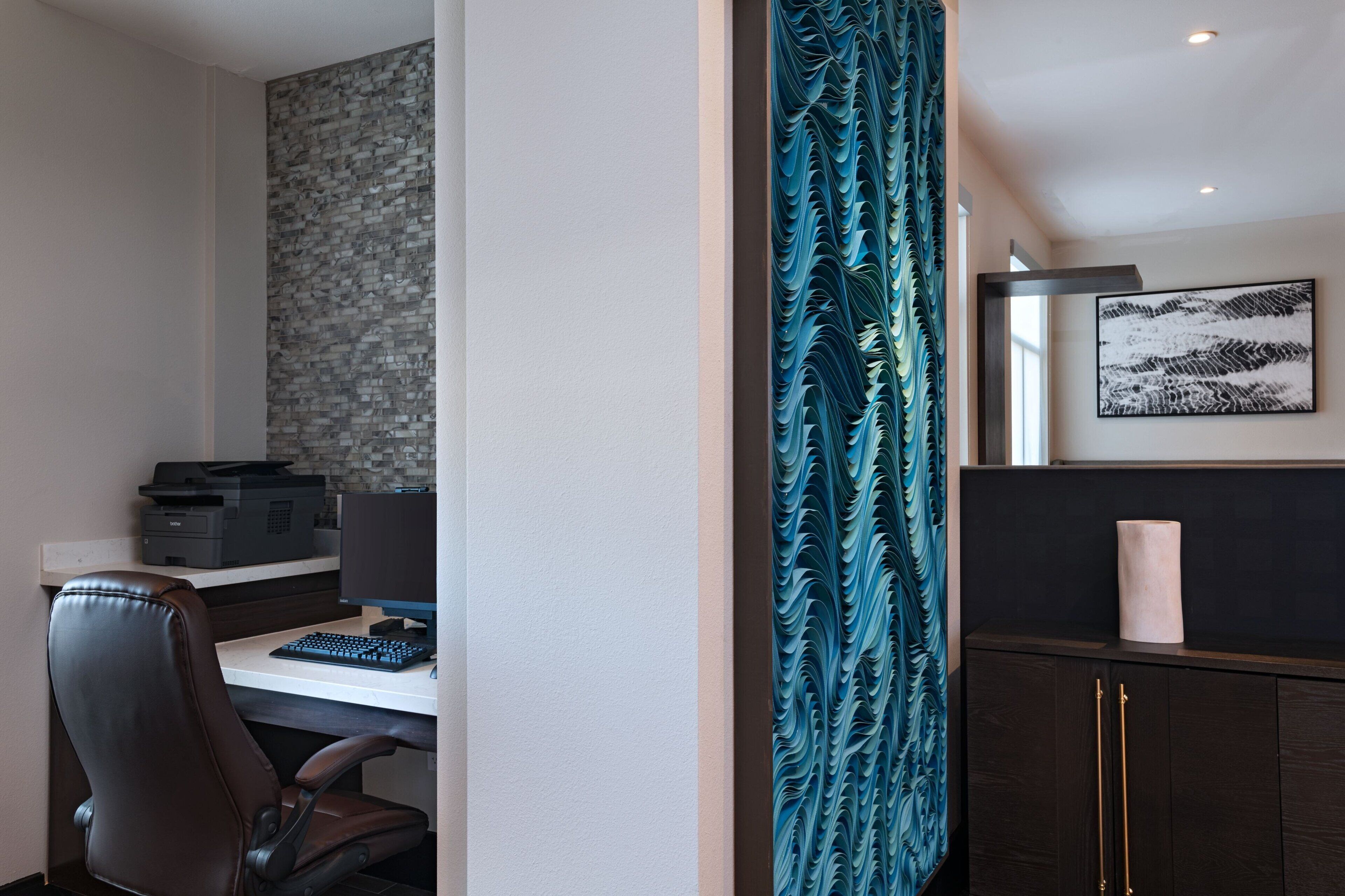 Um espaço de escritório moderno com escrivaninha, cadeira, impressora e painel decorativo na parede.
