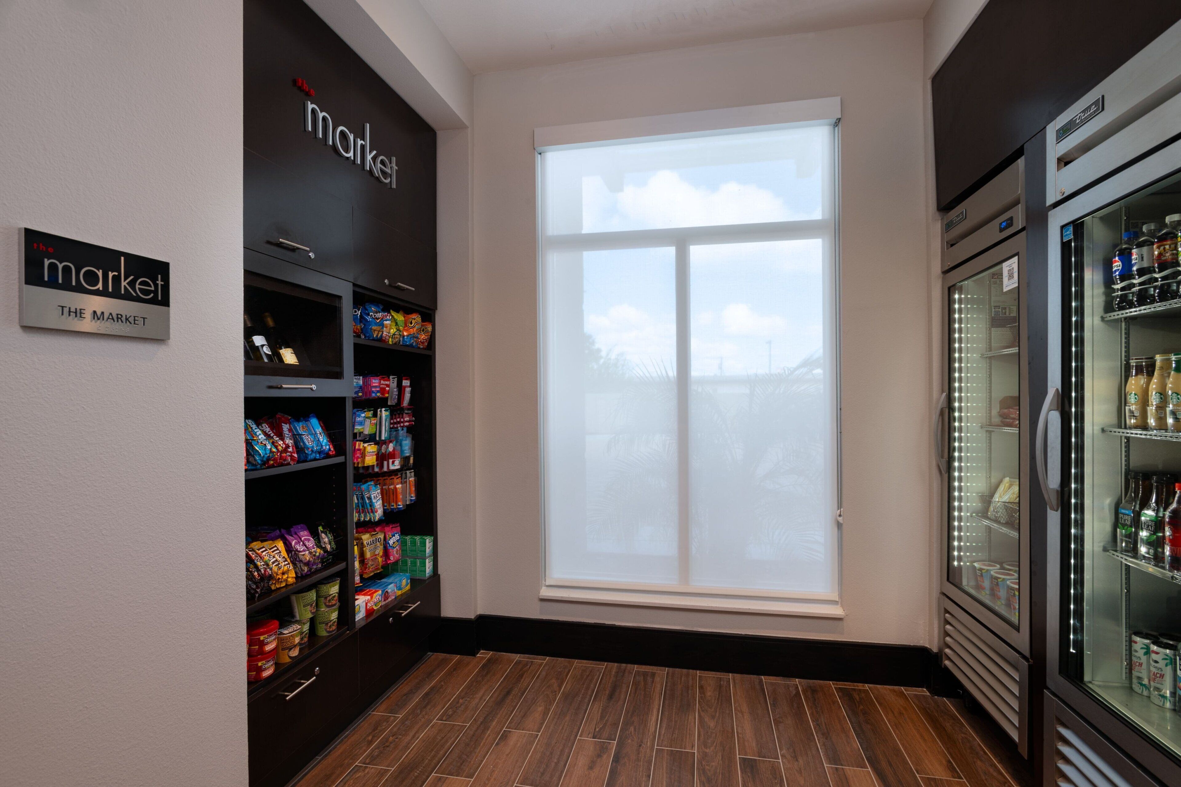 A store interior with shelves stocked with snacks and beverages, a large window, and a refrigerated display case.