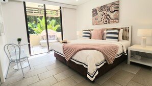A modern bedroom with a large bed, a bedside table, a chair, and a view of the outdoors. - Luxury Spa Suite #220 Temple Palm Cove (Palm Cove)