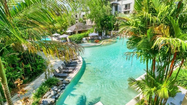 A swimming pool with lounge chairs and palm trees, surrounded by a resort building. - Luxury Spa Suite #220 Temple Palm Cove (Palm Cove)