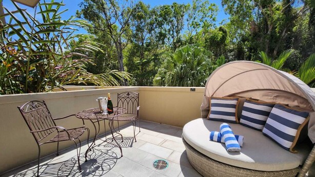 A patio with a round wicker sofa, metal chairs, and a table with a bottle and glass. - Luxury Spa Suite #220 Temple Palm Cove (Palm Cove)