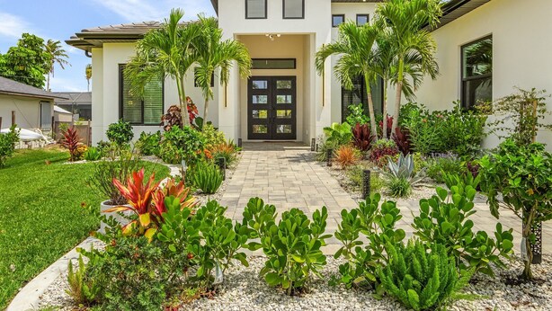 Une maison moderne avec une allée pavée, entourée de différentes plantes et d’une pelouse bien entretenue.