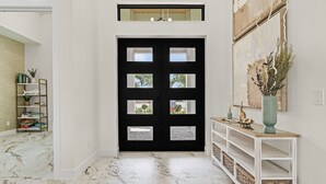 Un couloir avec une porte noire, des étagères blanches et un sol en marbre.