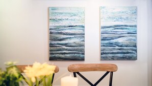 Two abstract paintings on a wall, a wooden chair, and a vase with flowers on a table.