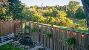 A wooden deck with a white picket fence, a small bridge, and string lights.