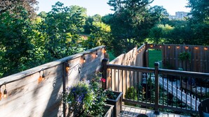 A wooden deck with string lights, surrounded by lush greenery and a white fence.
