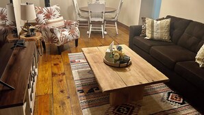 A cozy living room with a wooden coffee table, a brown sofa, and a dining area with a white table and chairs. - 🏡Little Bear Cabin In Helen🐻 (Helen)