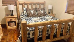 A wooden bed with a checkered bedspread and multiple pillows, flanked by nightstands with lamps and a small basket. - 🏡Little Bear Cabin In Helen🐻 (Helen)